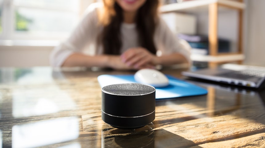 Close up of a smart speaker in front of a Genz woman blurred in the background